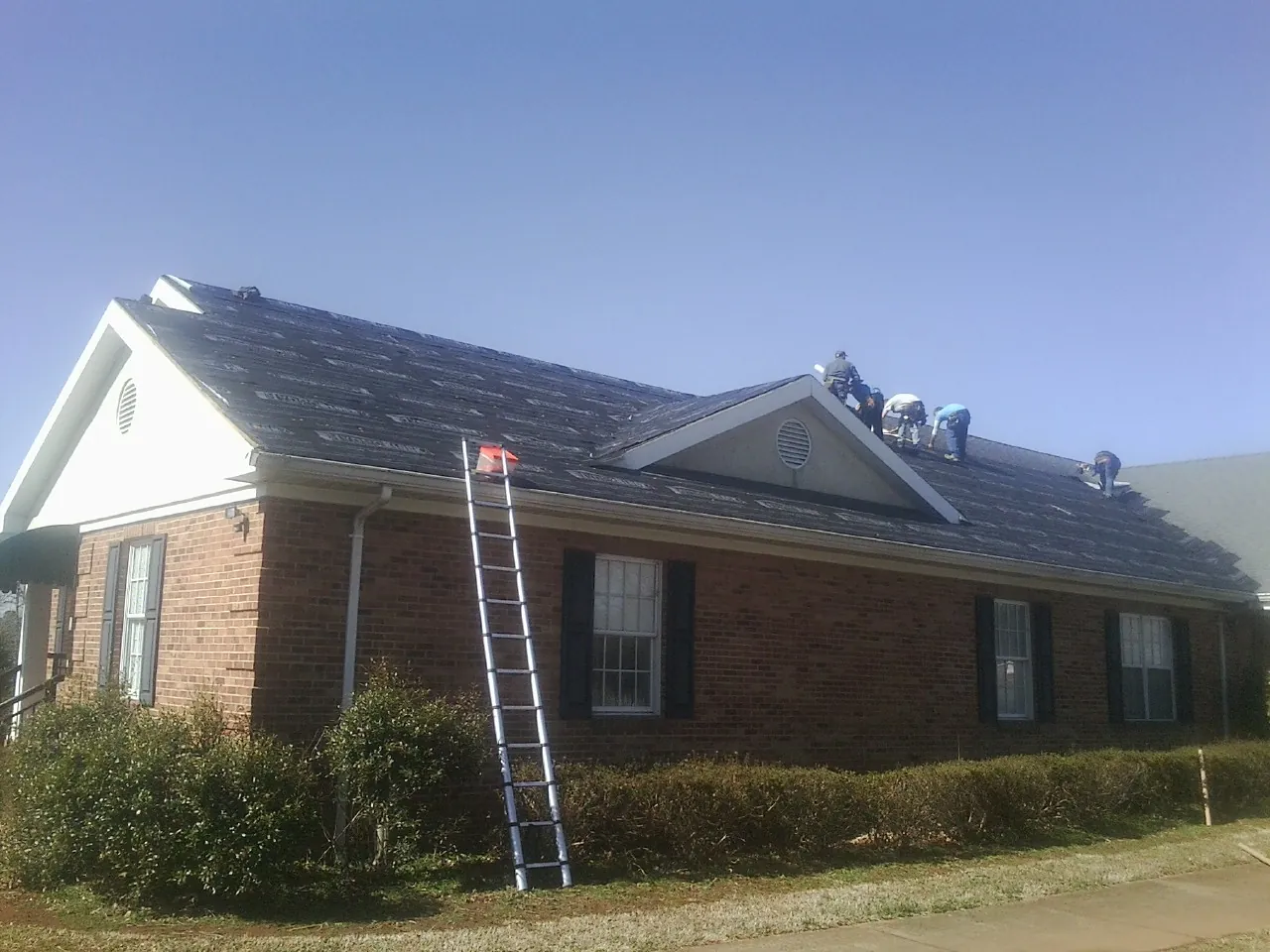 Crew tearing shingles off a brick ranch roof with a ladder set — Metal Roof Repair work by our crew in Shepherdsville