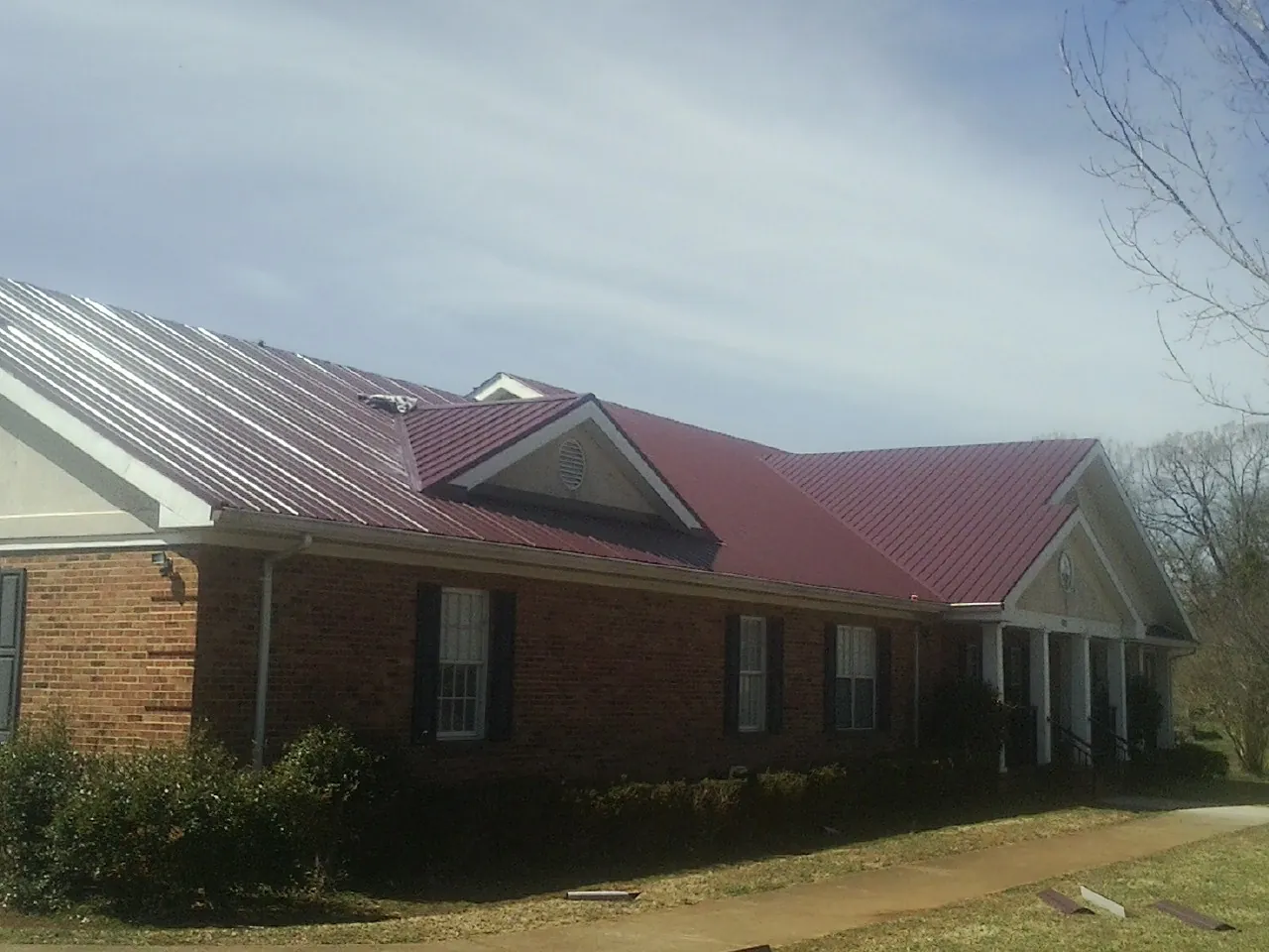 Red metal roof with gabled entries on a long brick building, from a Hail Damage Roof Repair job in Shepherdsville