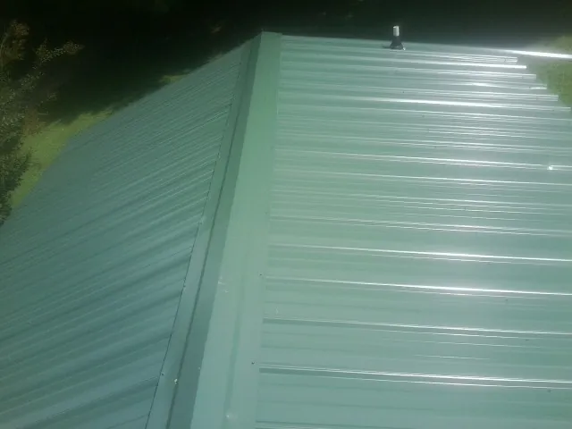 New green metal panels meeting at the ridge of a roof — Flat Roof Repair work by our crew in Shepherdsville