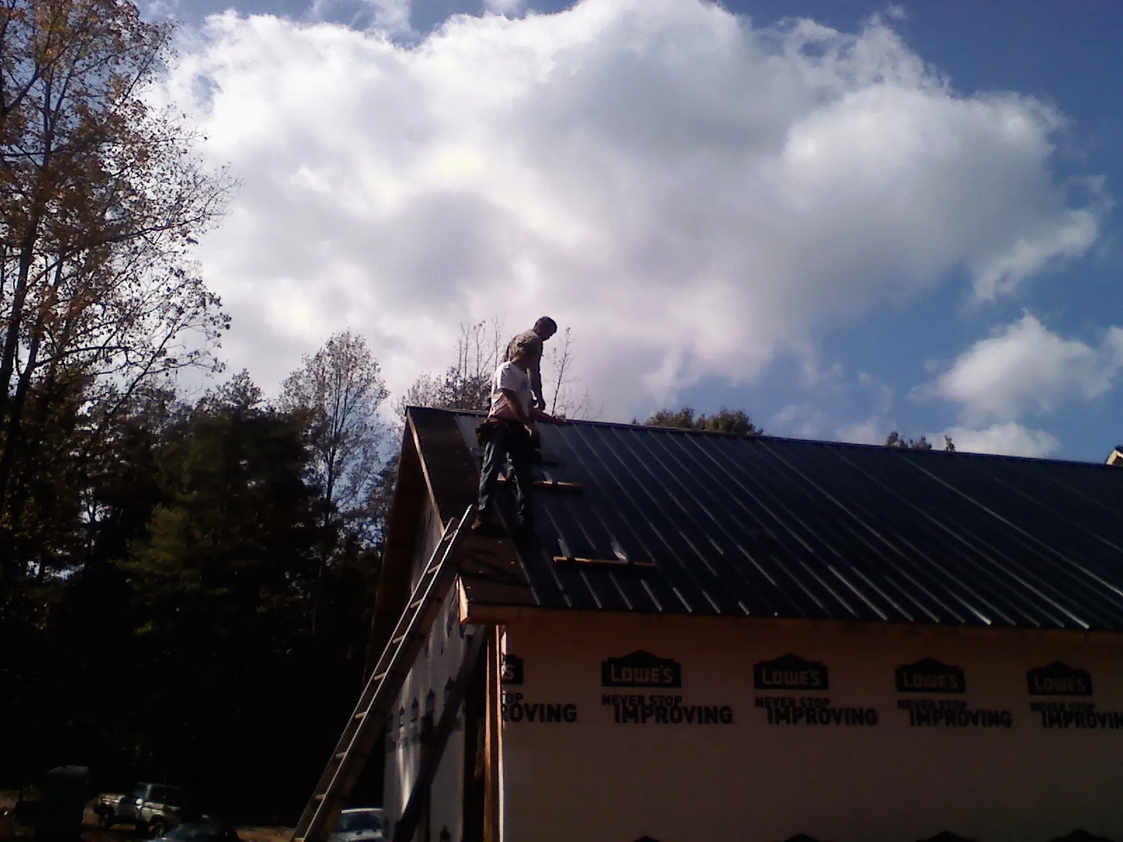Roofer fastening dark metal panels high against a cloudy sky, from a Roof Inspection job in Shepherdsville
