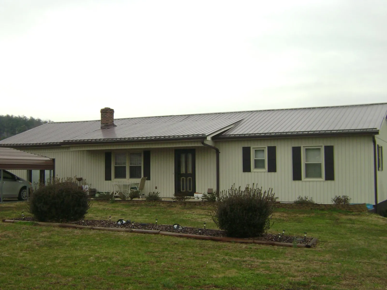 Brown metal roof on a cream sided ranch home with a brick chimney in Shepherdsville
