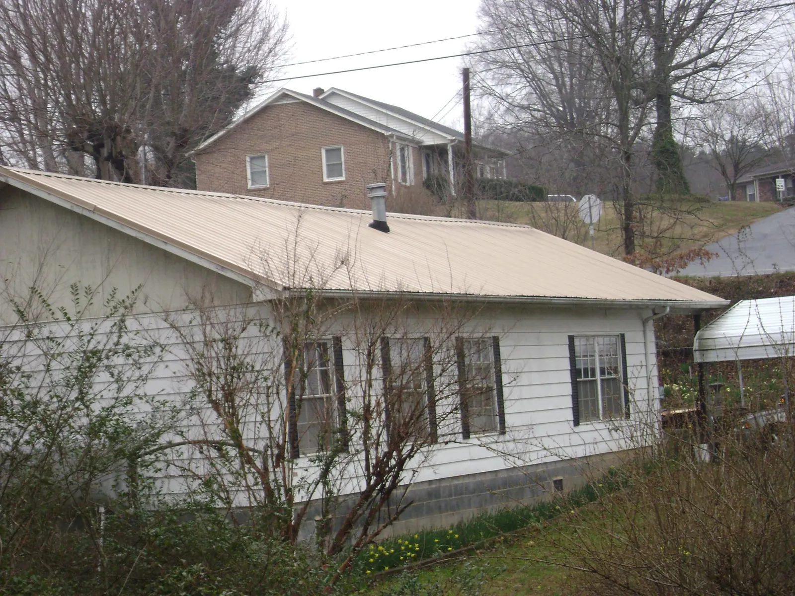 Tan metal roof on a white sided house set into a hillside — Commercial Roofing by Roofing Brothers in Shepherdsville
