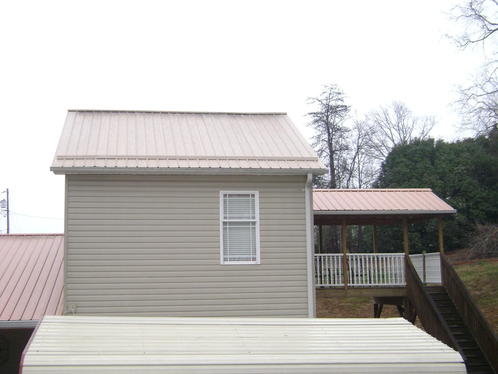 Tan metal roofs on a two story addition and attached porch, from a Roof Replacement job in Shepherdsville